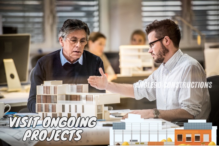 Two professionals discussing a building model in an office, highlighting the importance of visiting ongoing projects. Angle90 Constructions in Coimbatore welcomes you to explore our current works to understand our commitment to quality